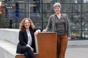Miriam van Koningsbruggen en Kirsti Jakobs zitten en staan buiten bij een koperen bank.
