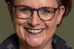 Lachende vrouw met kort donker haar en bril.