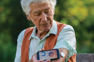 Oudere man met meetinstrument en sensor op bovenarm.